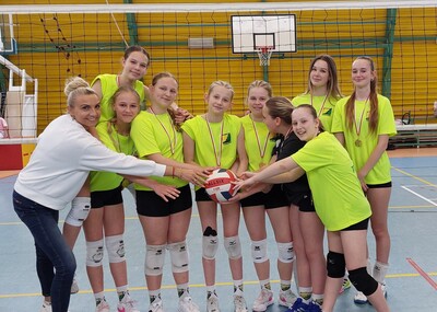 Drużyna siatkarska z dziewcząt z nauczycielem na hali sportowej.