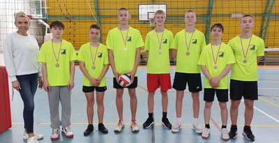 Drużyna siatkarska męska z nauczycielem na hali sportowej.