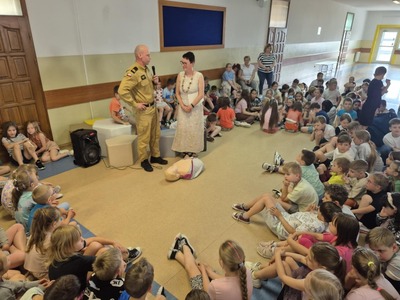 Pani dyrektor wraz z zaproszonym strażakiem na korytarzu szkolnym w otoczeniu uczniów klas 1-4