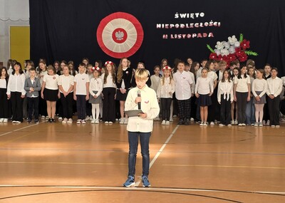 Uczeń klasy trzeciej w stroju galowym  występujący przed zgromadzoną społecznością szkolną.