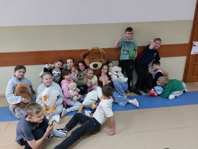 Zdjęcie grupowe uczniów na korytarzu szkolnym z pluszowymi misiami.
