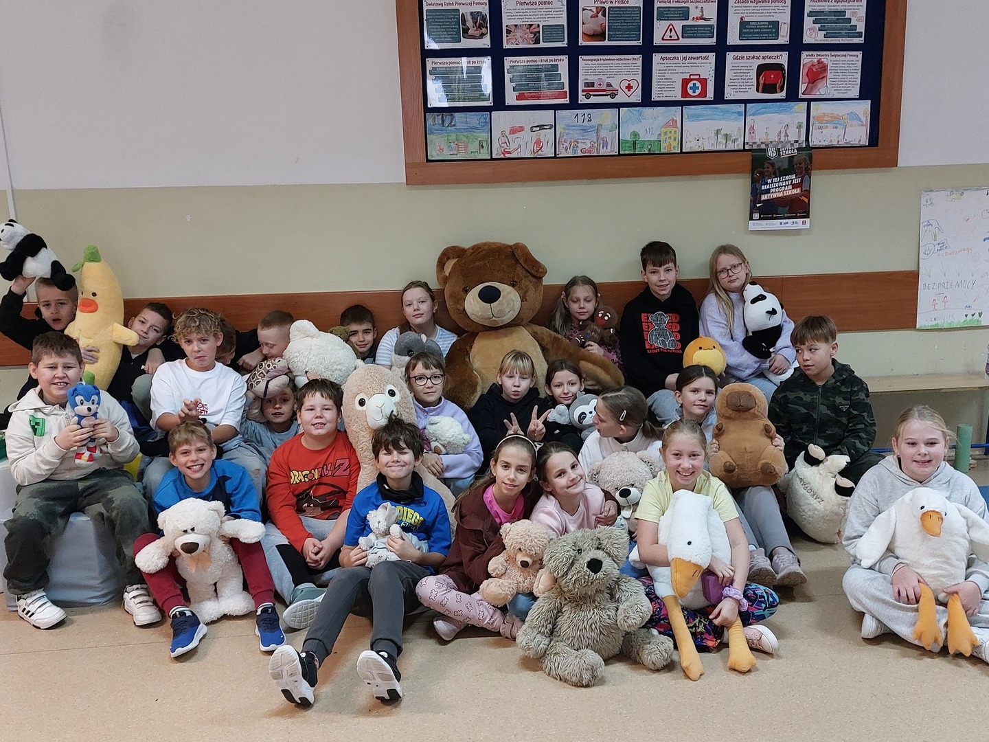Zdjęcie grupowe uczniów na korytarzu szkolnym z pluszowymi misiami.