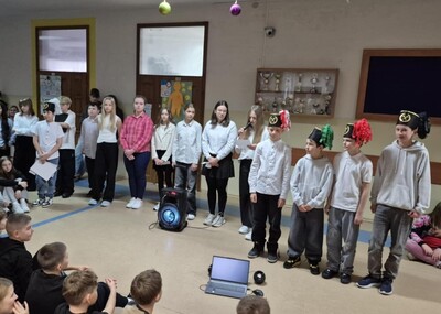 Uczniowie w strojach galowych przed społecznością szkolną podczas akademii.