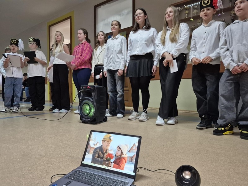 Uczniowie w strojach galowych przed społecznością szkolną podczas akademii.