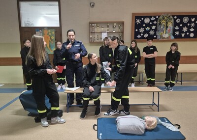 Uczniowie  w strojach strażackich na holu szkoły występujący przed zgromadzonymi uczestnikami apelu.