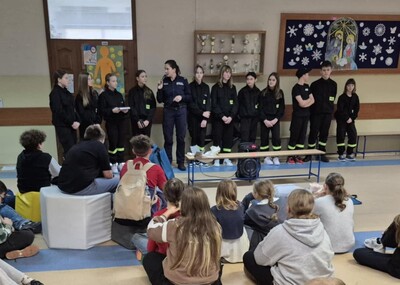 Uczniowie  w strojach strażackich na holu szkoły występujący przed zgromadzonymi uczestnikami apelu.