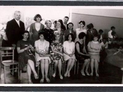 Nauczyciele pozujący do zdjęcia w sali szkolnej. W pierwszym rzędzie część nauczycieli siedzi, za nimi stoi pozostała kadra pedagogiczna, w tle dzieci.