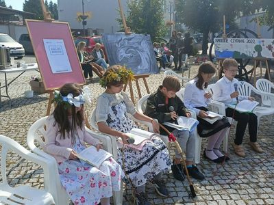 Pięcioro uczniów klas piątych, w tym dwie uczennice w strojach świtezianek, siedzi na krzesłach i czytają fragmenty Ballad i romansów Mickiewicza.