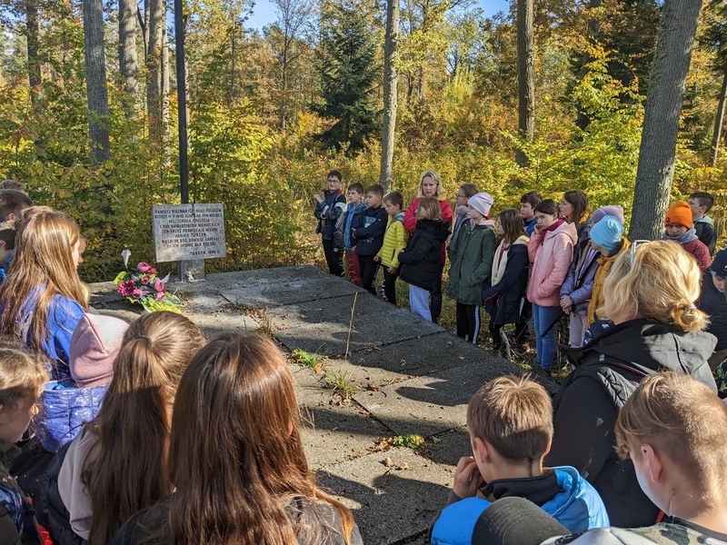 Uczniowie klas piątych wraz z opiekunami zgromadzeni przy leśnej mogile nieznanego żołnierza.