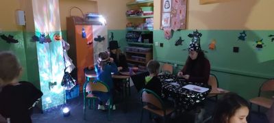 Świetlica. Przy dwóch stolikach wróżki, uczniowie i uczennice, którym przepowiadana jest przyszłość. W tle przyklejone nietoperze, dynie oraz wróżki.