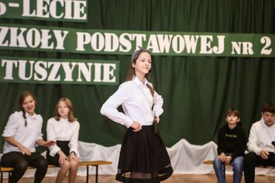Scena na sali gimnastycznej. W centralnej części uczennica śpiewająca do mikrofonu. W tle czworo aktorów. 