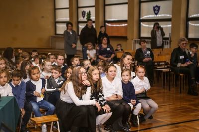 Widownia. Po lewej stronie, na niskich ławkach siedzą dzieci z klas od 1 do 5. Po stronie prawej nauczyciele edukacji wczesnoszkolnej.