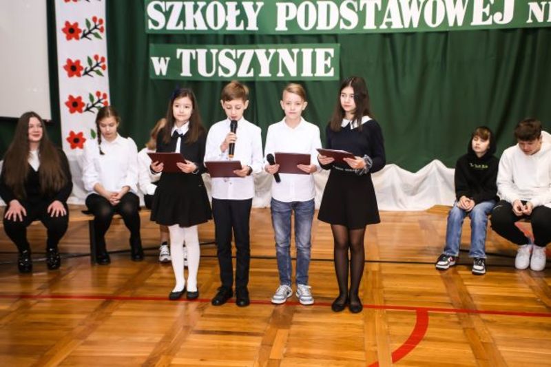 Czworo dzieci na środku sali. Wszyscy ubrani w stroje galowe. W rękach trzymają mikrofony.