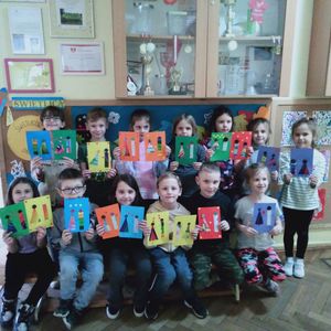Grupa dzieci świetlicowych trzymająca w rękach, przygotowane przez siebie, laurki z okazji Dnia Babci i Dziadka.