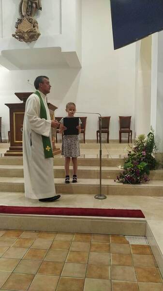 Wnętrze kościoła. Na środku dziewczynka przy mikrofonie. Na lewo ksiądz.