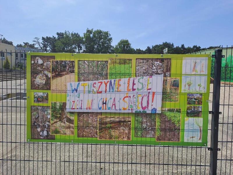 Baner na ogrodzeniu szkoły z hasłem "W Tuszynie Lesie dzieci nie chcą śmieci".