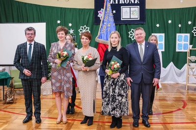 Na środku sali gimnastycznej grupa 5 osób, w tym między innymi Dyrektor Szkoły i Burmistrz Miasta Tuszyna, pracownice Urzędu Miasta trzymają kwiaty.