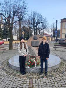 Dziewczynka i chłopiec składają wiązankę pod pomnikiem Reymonta w Tuszynie, kwiaty na wiązance w kolorze biało-czerwonym