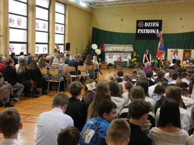 Goście i uczniowie w sali gimnastycznej, sztandar, dekoracja – stara chłopska chata