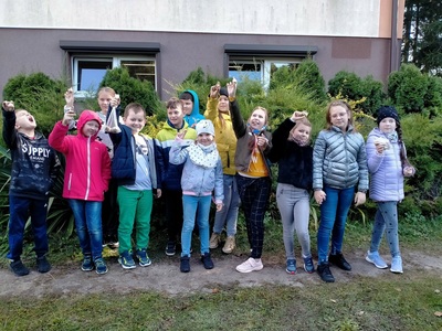 Uczniowie z klasy III w dniu sadzenia cebulek żonkili. Dzieci stoją w ogrodzie na tle budynku szkoły