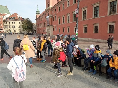 Grupa uczniów z opiekunami na Placu Zamkowym Warszawie.