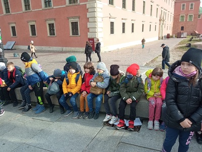 Grupa z klasy II siedząca na murku na Placu Zamkowym w Warszawie.
