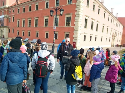 Grupa uczniów z przewodnikiem na Placu Zamkowym w Warszawie.