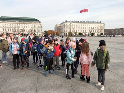 Grupa dzieci z opiekunami i przewodnikiem na Placu marszałka Józefa Piłsudskiego w Warszawie.