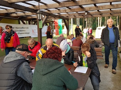 Kilkanaście osób siedzi przy stołach i pisze testy.