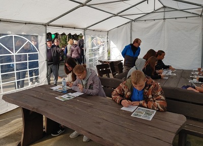 Kilka osób siedzi przy stołach i rozwiązuje zadania.