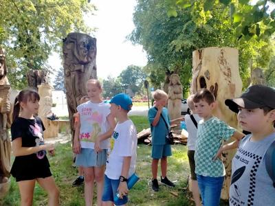 Grupa dzieci stoi, za nimi stoją rzeźby