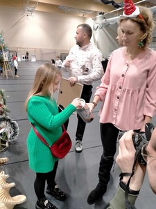 Dziewczynka wrzuca pieniążka do puszki, która trzyma nauczyciel, z tyłu jest pan.
