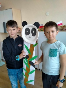 Dwóch chłopców trzyma pandę wykonaną z papieru.
