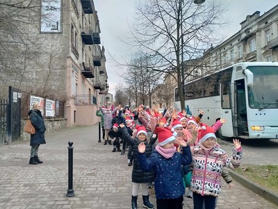Uczniowie klas 0-III w czapkach Mikołaja, stoją parami i machają