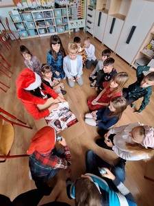 Dzieci siedzą na podłodze w kręgu nauczyciel rozdaje im prezenty.