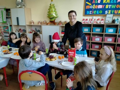Dzieci siedzą przy wigilijnym stole za nimi stoi nauczycielka.