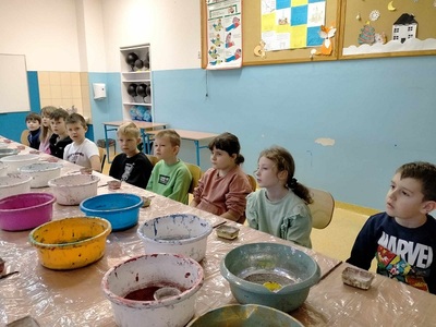 Dzieci siedzą przy stole, na którym stoją miski z brokatem..