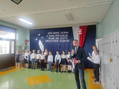 Społeczny Zastępca Dyrektora Szkoły przemawia do mikrofonu. Z tyłu stoją uczniowie.