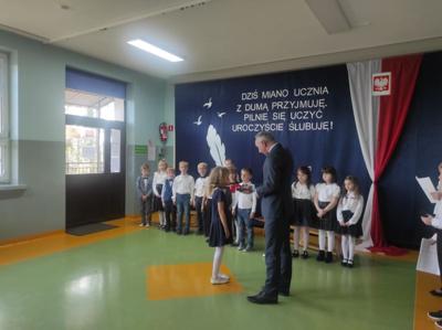 Społeczny Zastępca Dyrektora Szkoły pasuje uczennicę przykładając ołówek do jej ramienia.
