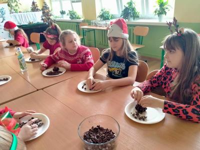 Uczniowie z klasy trzeciej siedzą przy stole i wykonują szyszkę
