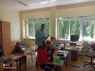 nauczyciel i uczniowie siedzący przy ławkach