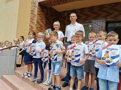 Dzieci trzymają dyplomy, stoją przed szkołą