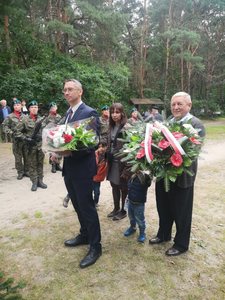 dwie osoby trzymają kwiaty, w tle grupa żołnierzy