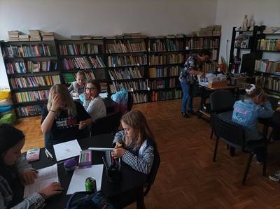 dzieci siedzą przy stolikach w bibliotece