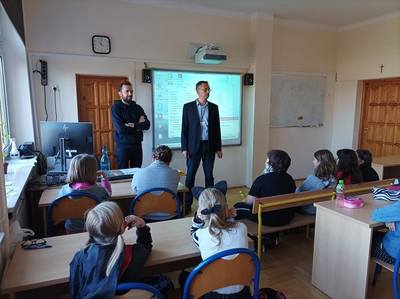 dyrektor mówi do uczniów siedzących w ławkach
