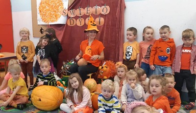 dzieci ubrane na pomarańczowo siedzą wśród dyń