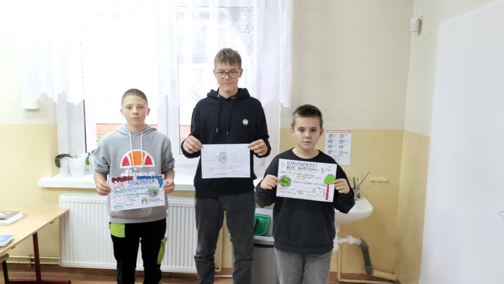 Na zdjęciu 3 chłopców trzymających w ręku plakaty przedstawiające Parki Narodowe w Polsce.