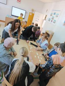 Na zdjęciu uczniowie i seniorzy podczas zajęć gry w Rummikuba wraz z nauczycielem. 