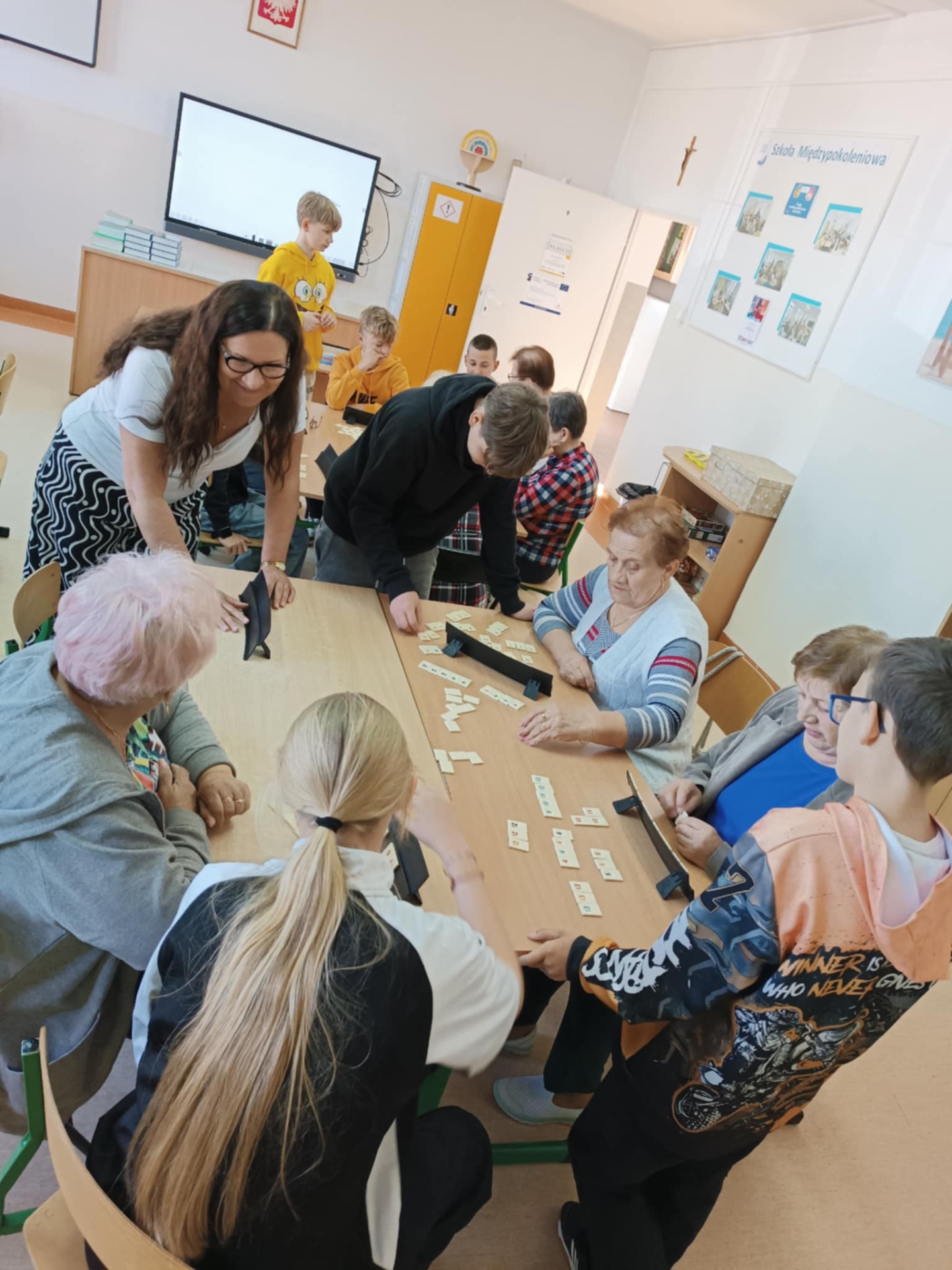 Na zdjęciu uczniowie i seniorzy podczas zajęć gry w Rummikuba wraz z nauczycielem.