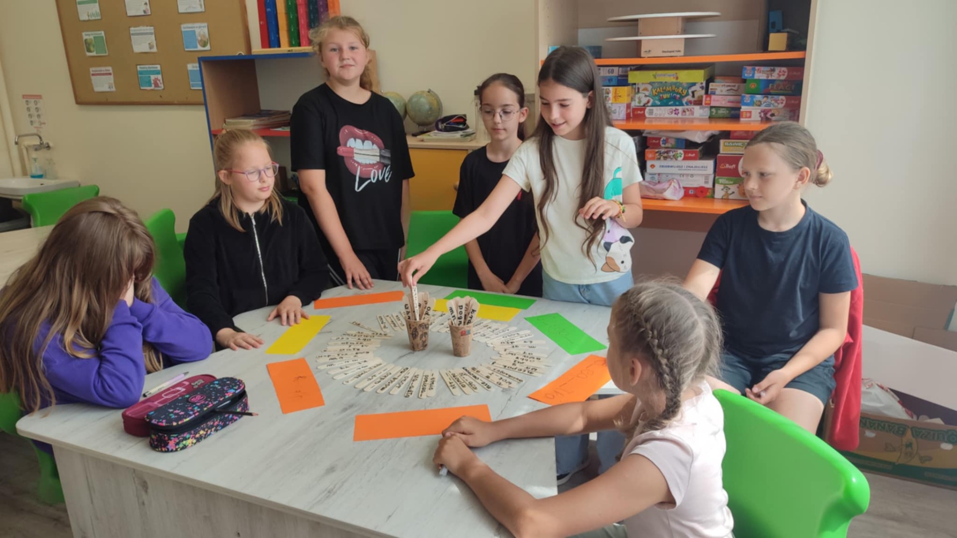 Na zdjęciu uczennice klasy 4. Dziewczynki losują pytania i rozwiązują zadania z języka polskiego. Dziewczynki w klasie. Uśmiechnięte.